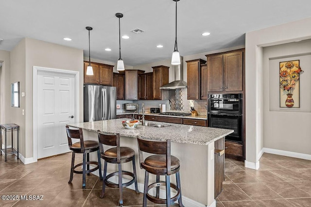 kitchen featuring visible vents, wall chimney exhaust hood, stainless steel appliances, tasteful backsplash, and a sink