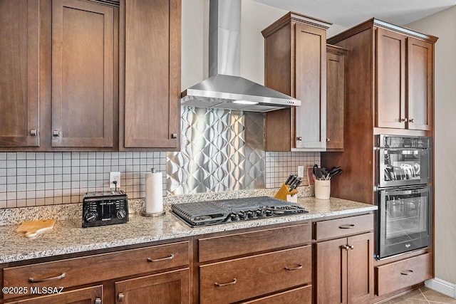 kitchen with double wall oven, backsplash, black gas cooktop, wall chimney exhaust hood, and light stone countertops