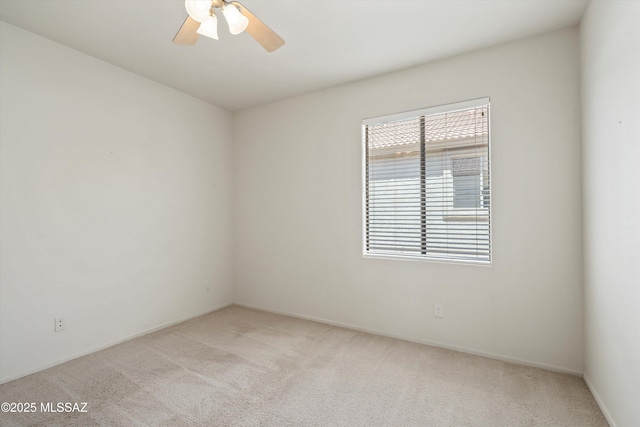 spare room featuring a ceiling fan, light colored carpet, and baseboards