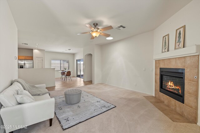 living area with a fireplace, a ceiling fan, visible vents, arched walkways, and light colored carpet