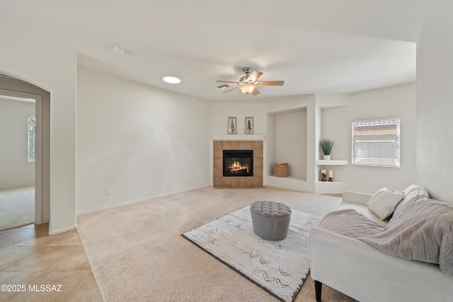 living area with ceiling fan, baseboards, arched walkways, light carpet, and a fireplace