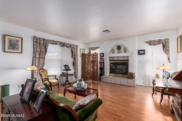 living room with a textured ceiling, visible vents, a tiled fireplace, and wood finished floors