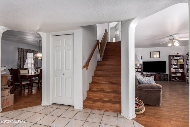stairway featuring arched walkways, a textured ceiling, ceiling fan, and tile patterned floors