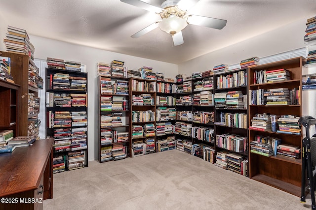 misc room with wall of books, carpet flooring, and a ceiling fan