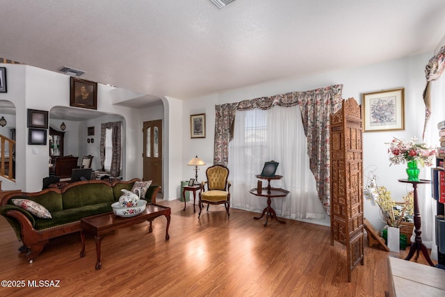 living room with arched walkways, wood finished floors, and visible vents