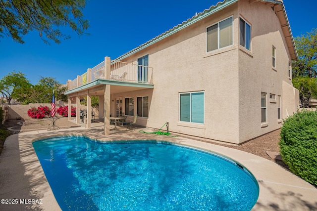 back of house featuring a patio, stucco siding, a balcony, and a fenced in pool