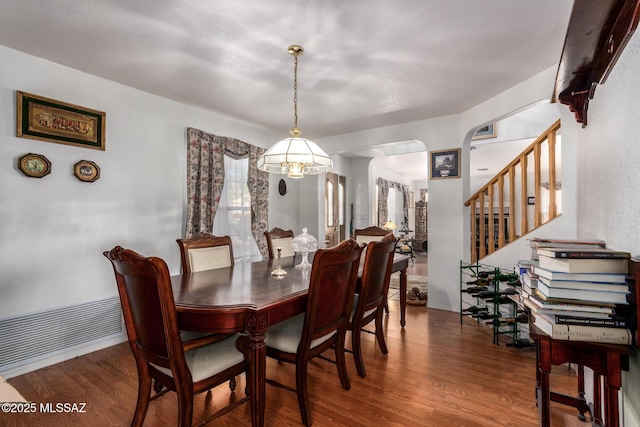 dining space featuring baseboards, arched walkways, stairs, and wood finished floors
