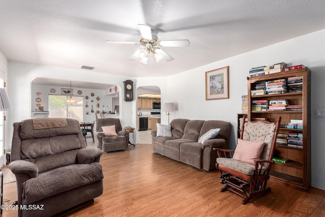 living room with visible vents, arched walkways, light wood-style floors, and ceiling fan