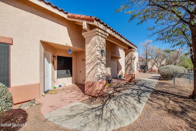 entrance to property with stucco siding, a tiled roof, and a patio area