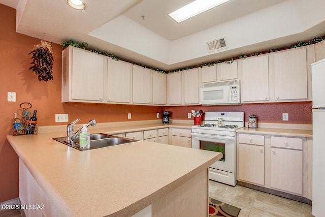 kitchen featuring light countertops, a sink, a peninsula, white appliances, and visible vents