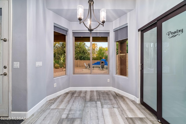 unfurnished dining area with baseboards, a notable chandelier, and wood finished floors