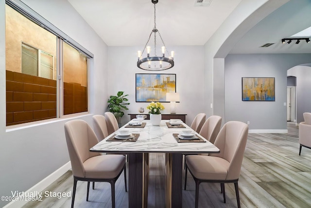 dining area with baseboards, light wood-style flooring, visible vents, and arched walkways