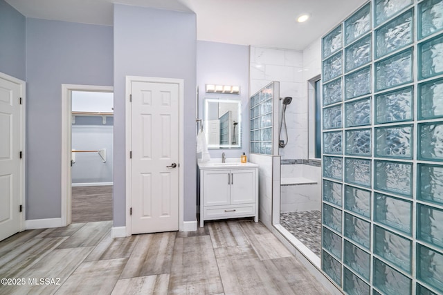 bathroom with wood finished floors, a walk in closet, vanity, walk in shower, and baseboards