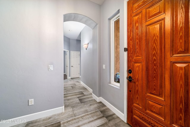 foyer with arched walkways, light wood-type flooring, and baseboards