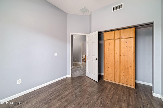 unfurnished bedroom featuring dark wood finished floors, baseboards, visible vents, and a closet