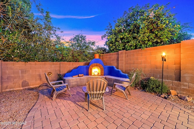 patio terrace at dusk with a fireplace and a fenced backyard