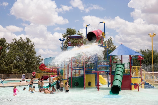 community jungle gym featuring a water play area, a community pool, and fence