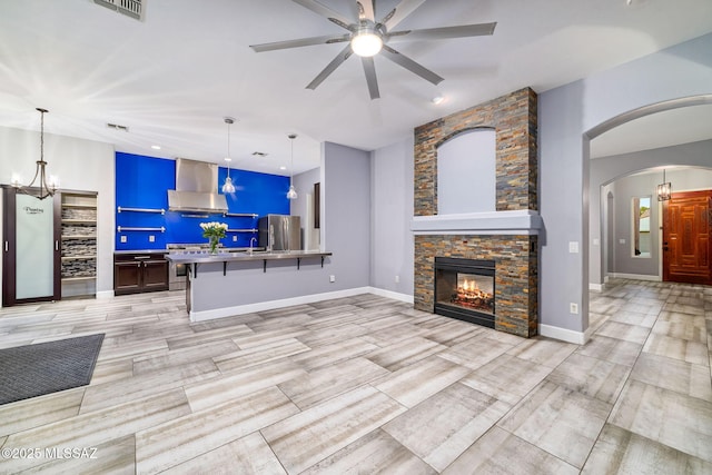 living room with a fireplace, arched walkways, visible vents, and ceiling fan with notable chandelier