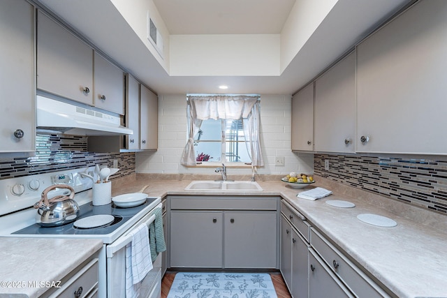 kitchen featuring white electric range, tasteful backsplash, under cabinet range hood, a sink, and gray cabinets
