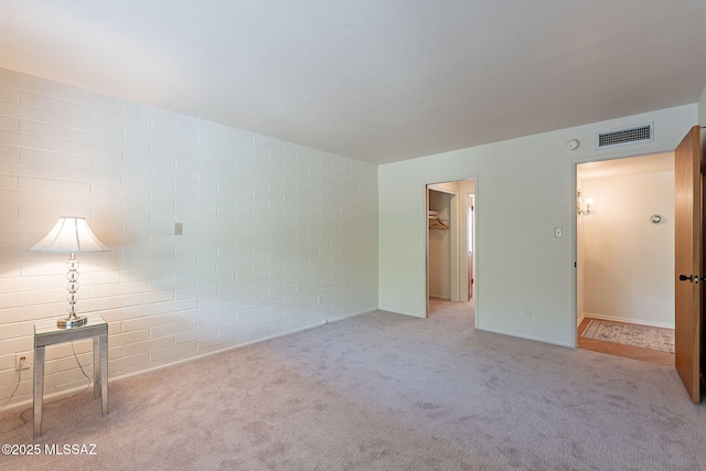 unfurnished room featuring carpet floors, visible vents, and brick wall