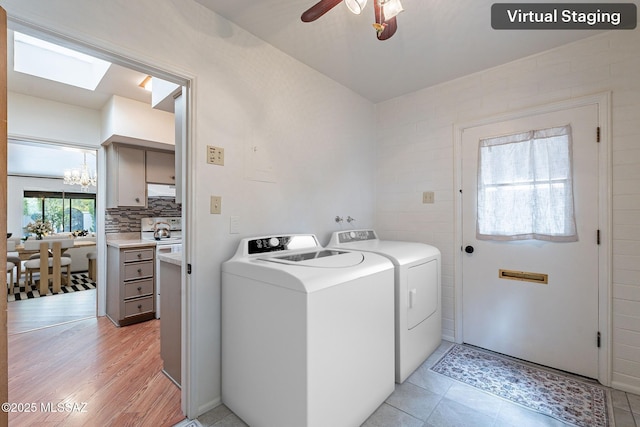 clothes washing area featuring separate washer and dryer, a skylight, ceiling fan with notable chandelier, and laundry area