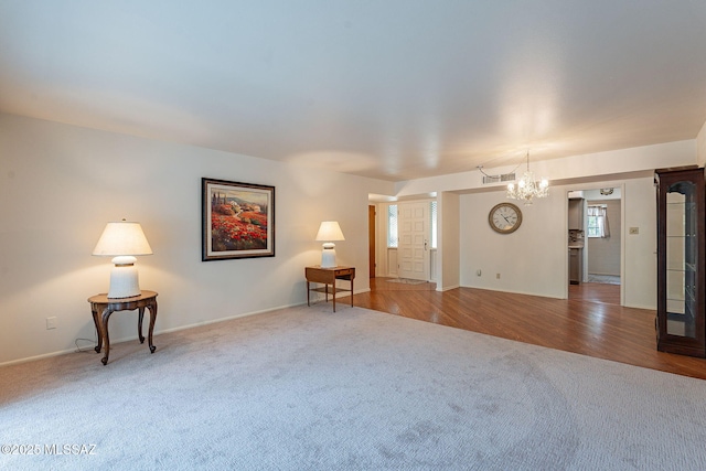unfurnished living room featuring baseboards, a chandelier, carpet floors, visible vents, and wood finished floors