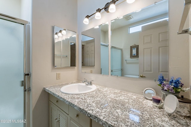 bathroom featuring a shower with door, visible vents, and vanity