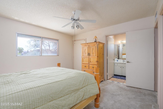 bedroom featuring ensuite bathroom, a textured ceiling, a ceiling fan, and light carpet