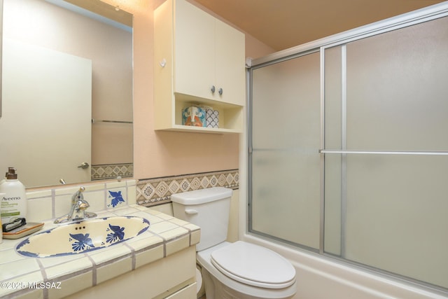 bathroom with a wainscoted wall, toilet, vanity, enclosed tub / shower combo, and tile walls