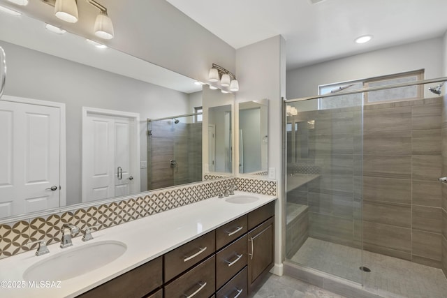 bathroom featuring double vanity, a sink, a stall shower, and tasteful backsplash