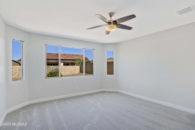 carpeted spare room with baseboards, visible vents, ceiling fan, and a wealth of natural light
