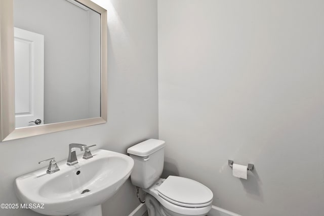 half bathroom featuring baseboards, a sink, and toilet
