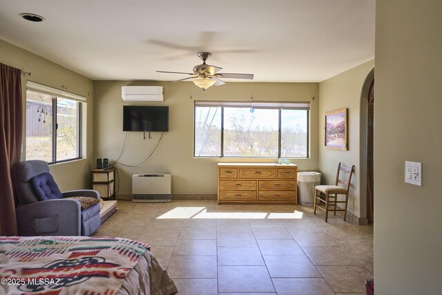 bedroom featuring light tile patterned floors, baseboards, arched walkways, a ceiling fan, and a wall mounted air conditioner