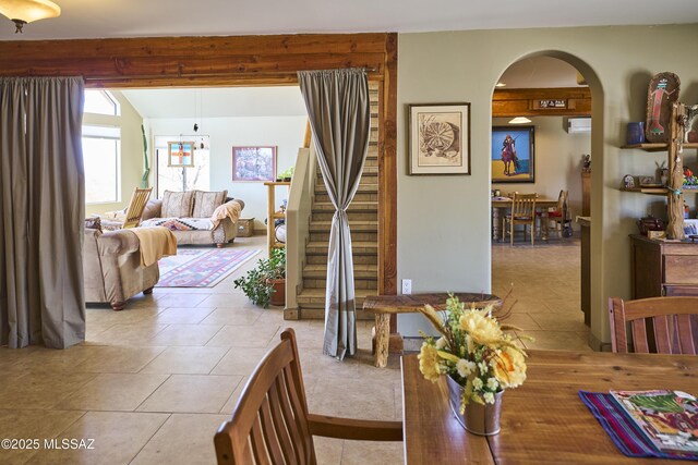 dining space with lofted ceiling with beams, tile patterned floors, arched walkways, and stairs