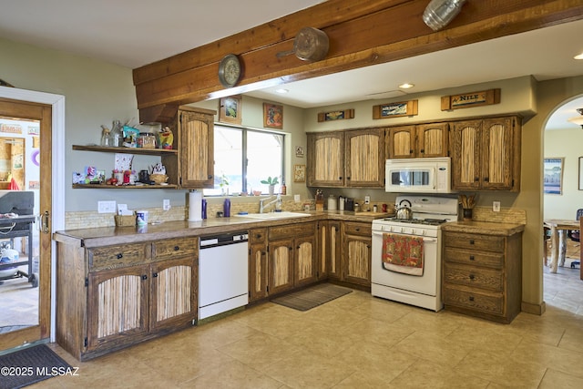 kitchen with white appliances, a sink, arched walkways, beam ceiling, and brown cabinetry
