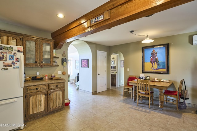 kitchen with baseboards, arched walkways, beamed ceiling, freestanding refrigerator, and glass insert cabinets