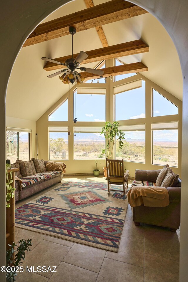 living area with arched walkways, a healthy amount of sunlight, beamed ceiling, and ceiling fan