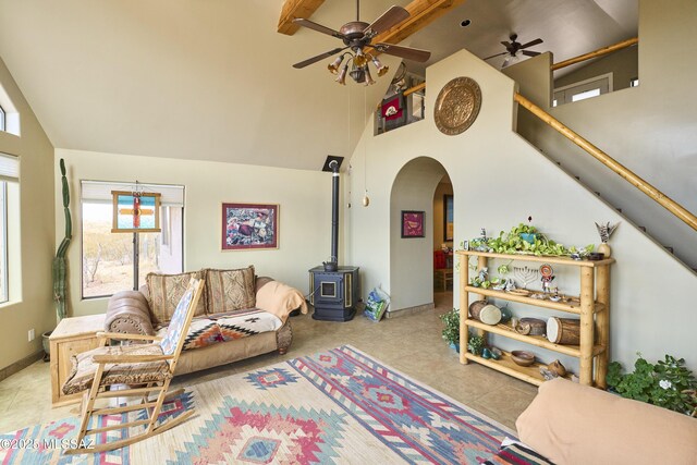 tiled living room featuring high vaulted ceiling, a ceiling fan, beam ceiling, arched walkways, and a wood stove