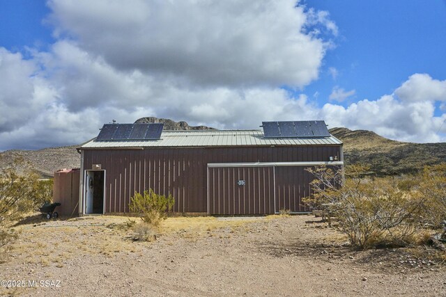 view of property exterior featuring an outbuilding, solar panels, a mountain view, and metal roof