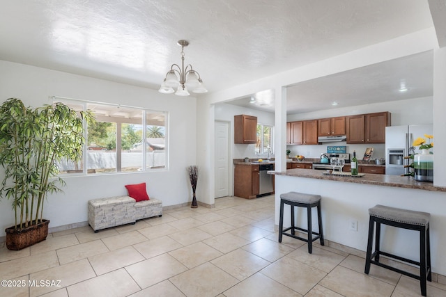 6517 E Cooper St, Tucson, AZ 85710 - kitchen featuring appliances with stainless steel finishes, under cabinet range hood, a breakfast bar area, brown cabinetry, and healthy amount of natural light