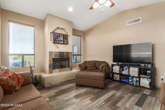 living area featuring lofted ceiling, visible vents, a ceiling fan, a tile fireplace, and wood finished floors