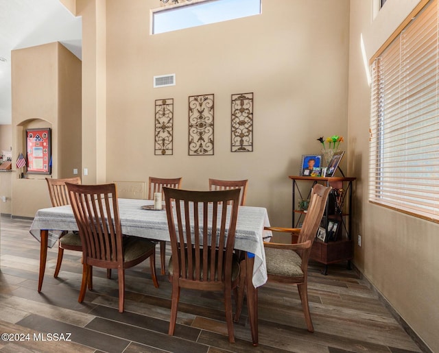 dining space featuring visible vents, wood finished floors, and a towering ceiling