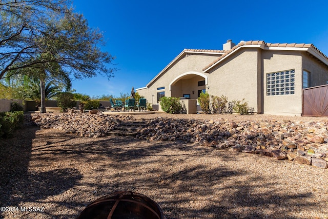 view of front facade with stucco siding, a chimney, fence, and a tiled roof