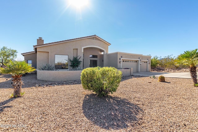 view of front of house with a tiled roof, a chimney, a garage, stucco siding, and driveway