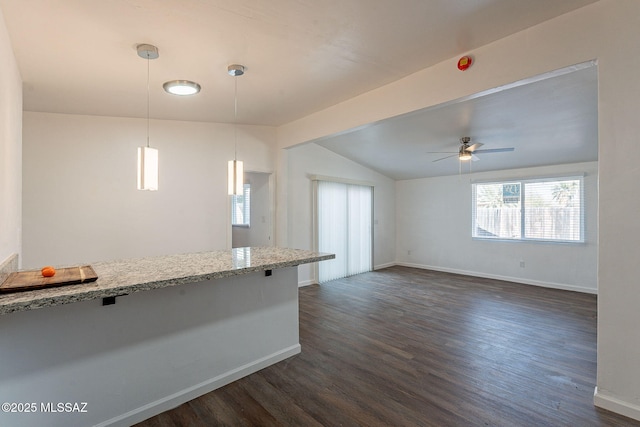 kitchen with lofted ceiling, dark wood-type flooring, baseboards, light stone counters, and pendant lighting