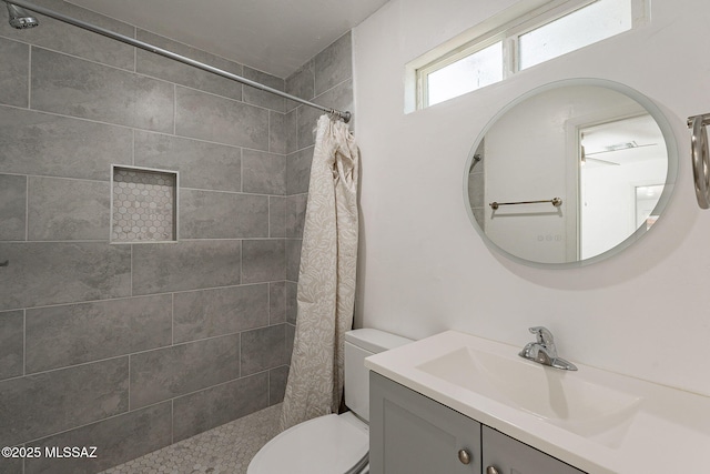 bathroom with toilet, a tile shower, and vanity