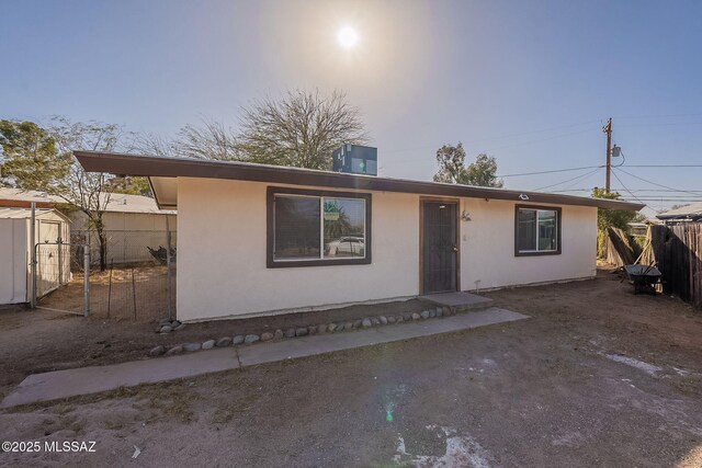 view of front facade with stucco siding, fence, an outdoor structure, and central AC unit