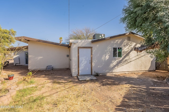 back of house with central AC unit and stucco siding