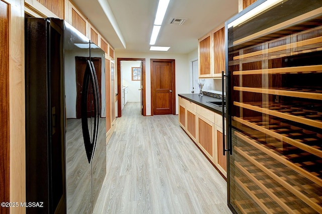 kitchen featuring beverage cooler, freestanding refrigerator, light wood-style floors, dark countertops, and visible vents