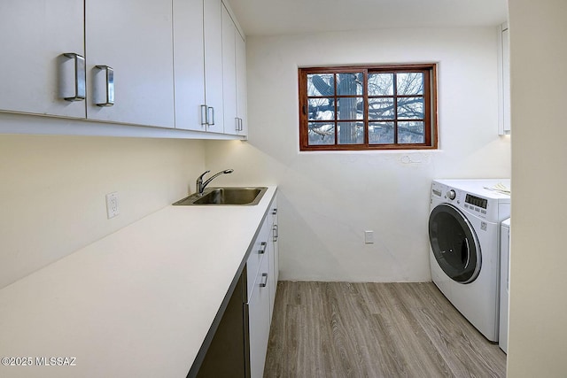 clothes washing area with cabinet space, washing machine and clothes dryer, light wood-style flooring, and a sink